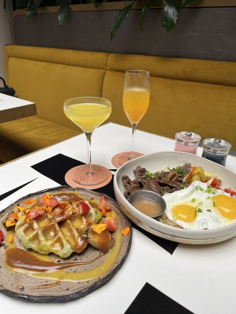 Brunch spread with waffles, eggs, and mimosas on a white table in a cozy café booth.