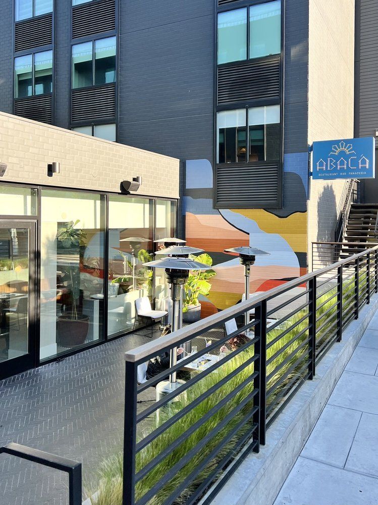 Modern building courtyard with glass storefronts, stairs, railings, umbrellas, and a blue sign.
