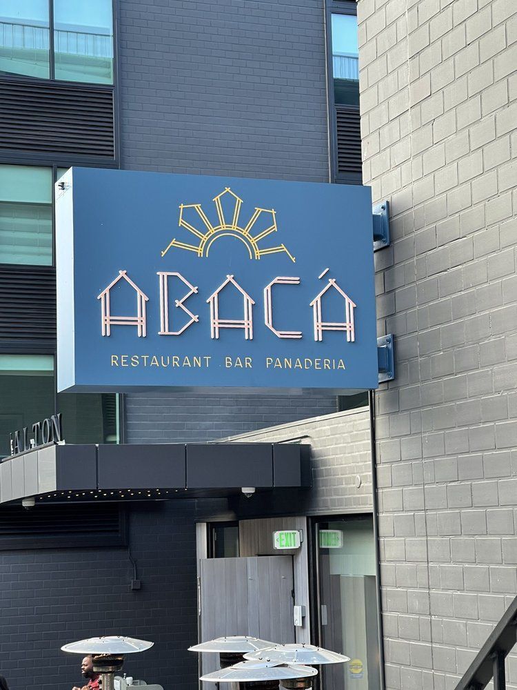 Blue sign for ABACA Restaurant & Bar Panadería on a brick building exterior.