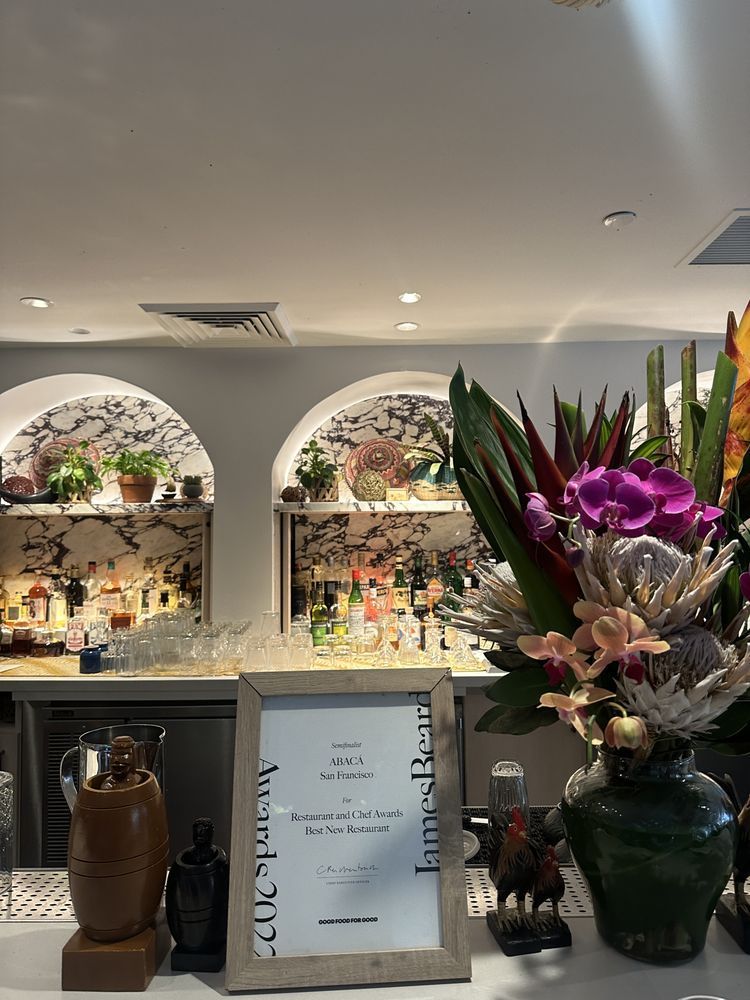 Restaurant counter with floral arrangements, glass display, and decorative alcoves on a softly lit wall