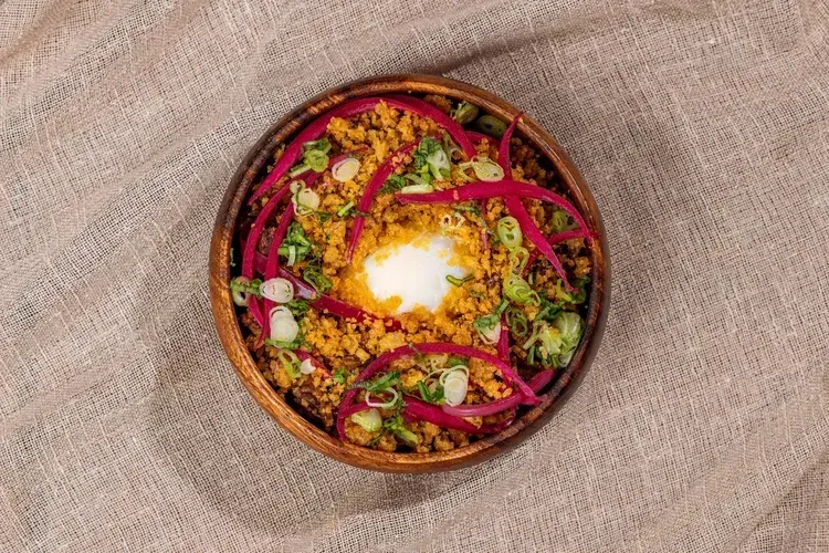 Colorful grain bowl with yogurt, vegetables, and herbs in a wooden bowl on a burlap cloth