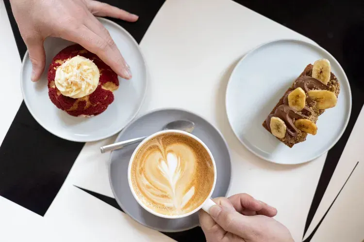 Top-down view of coffee, a berry pastry, and a dessert tart on white plates at a café table