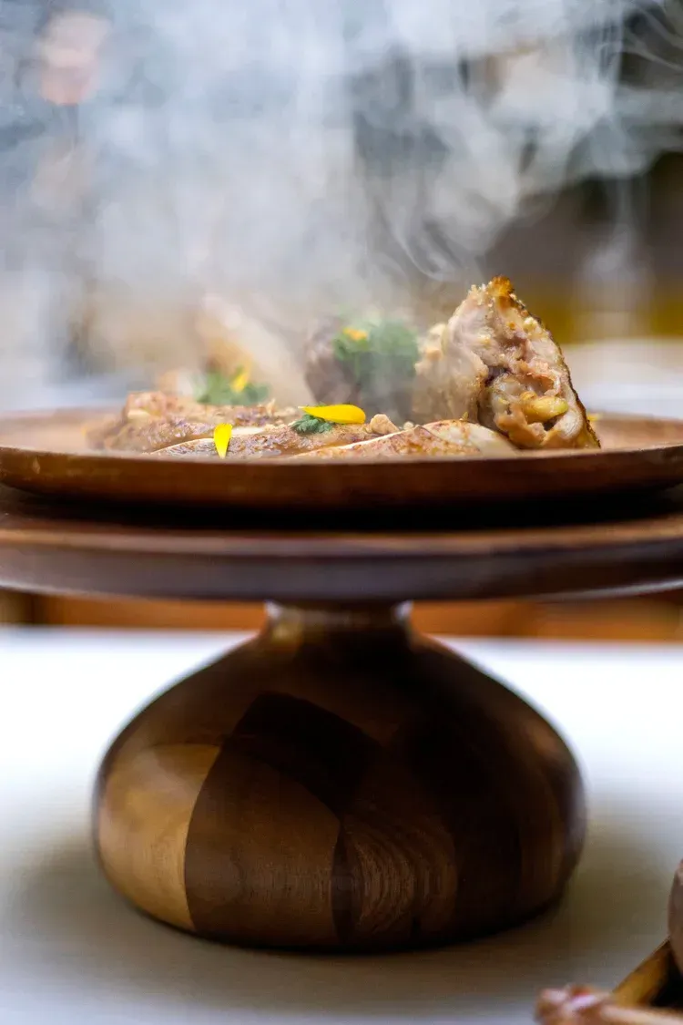 Steam rising from a plated gourmet dish on a wooden pedestal table.