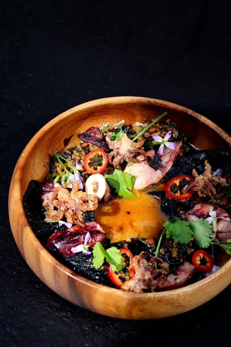 Wooden bowl of colorful noodle soup with herbs, sliced chilies, and a bright orange yolk center