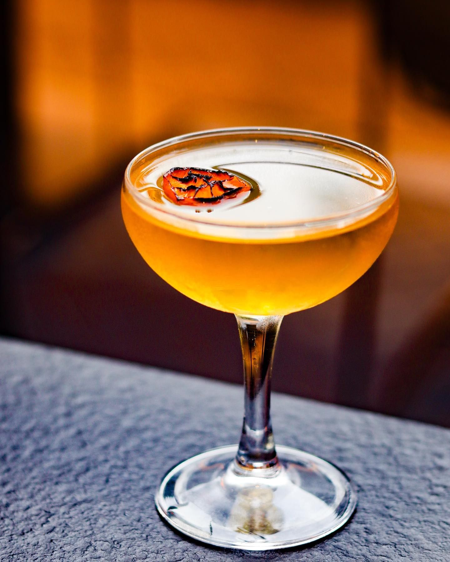Elegant amber cocktail in a coupe glass with a citrus garnish on a table