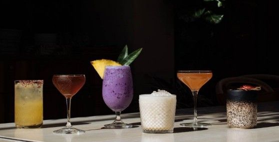 Assorted colorful cocktails and drinks lined up on a dark bar background