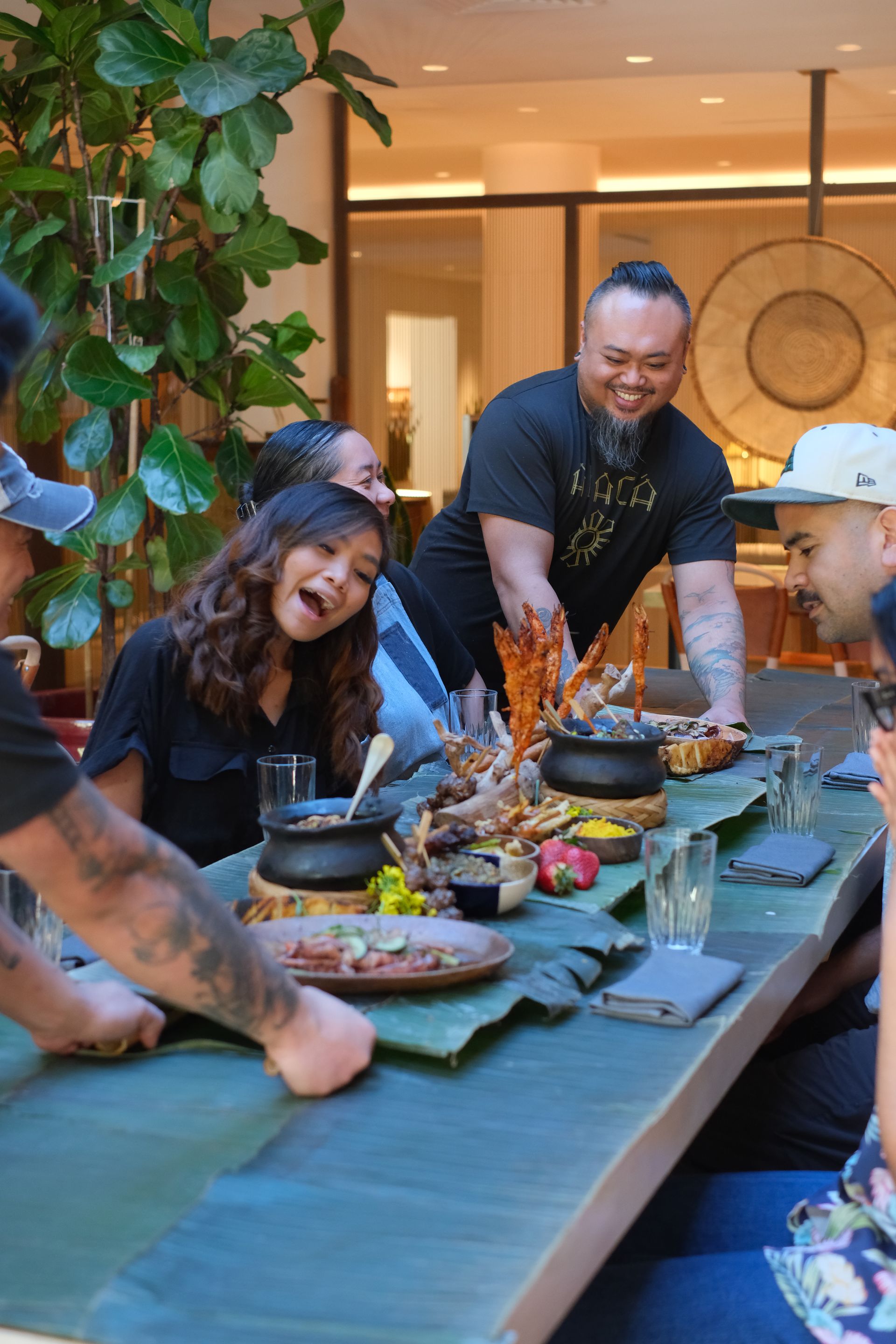 People sharing a meal at a long table indoors, smiling and serving food together