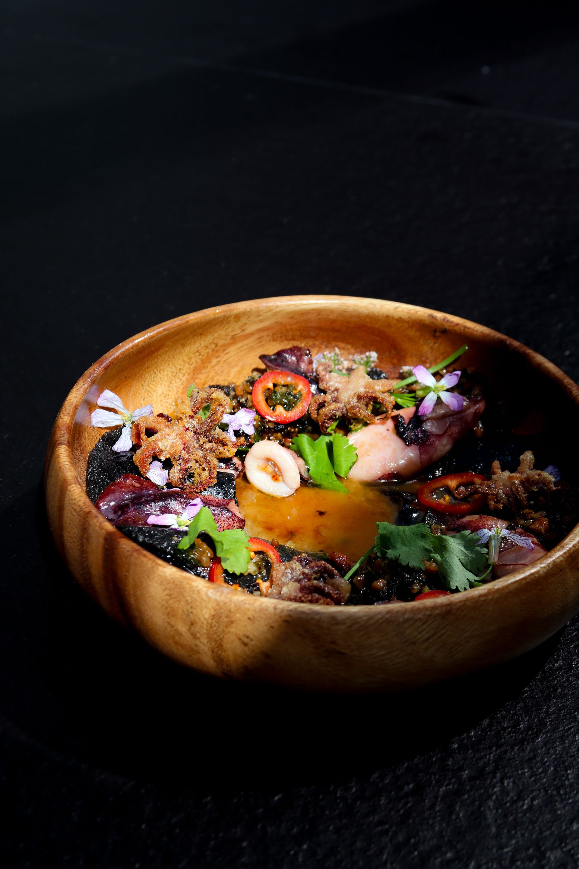 Wooden bowl of mixed salad with colorful vegetables and herbs on a dark background