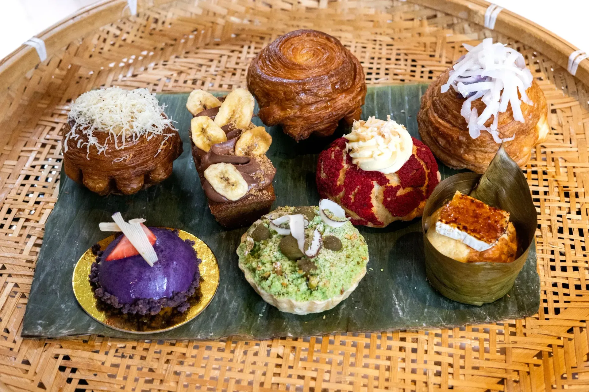 Assorted colorful bite-sized desserts on a woven tray, including purple, green, red, and white-topped sweets.