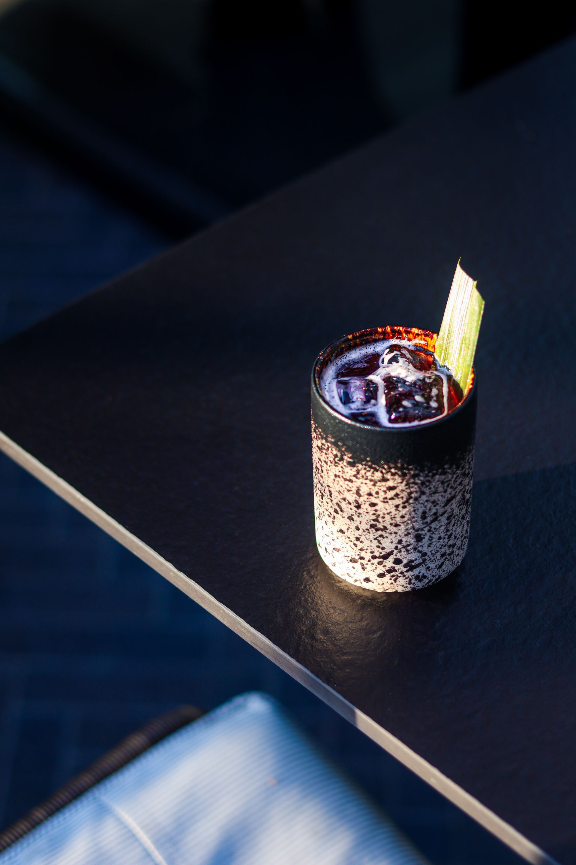 Cocktail in a speckled glass on a dark tabletop, garnished with a lemon peel and ice.
