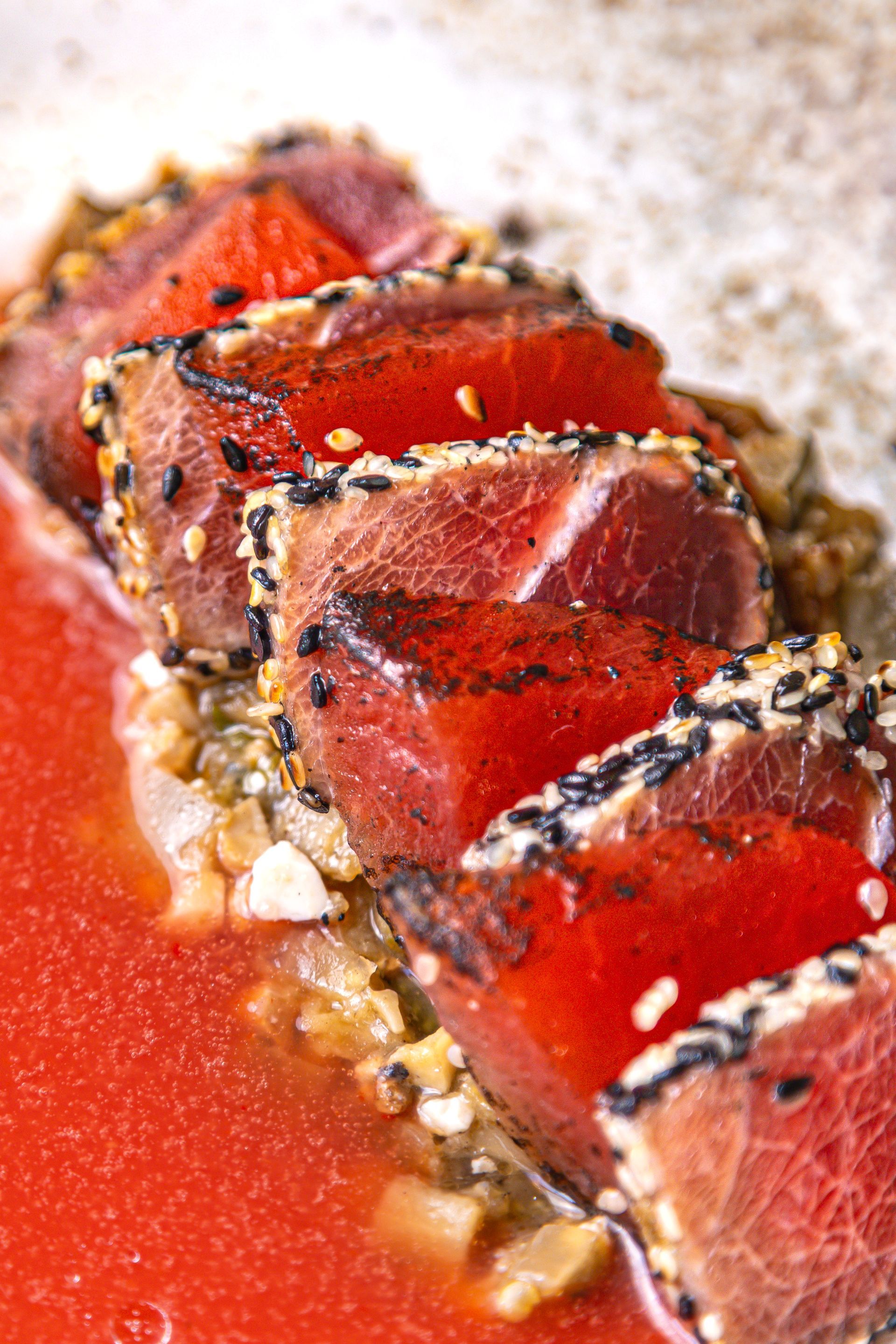 Sliced seared tuna with black sesame crust on a red sauce background