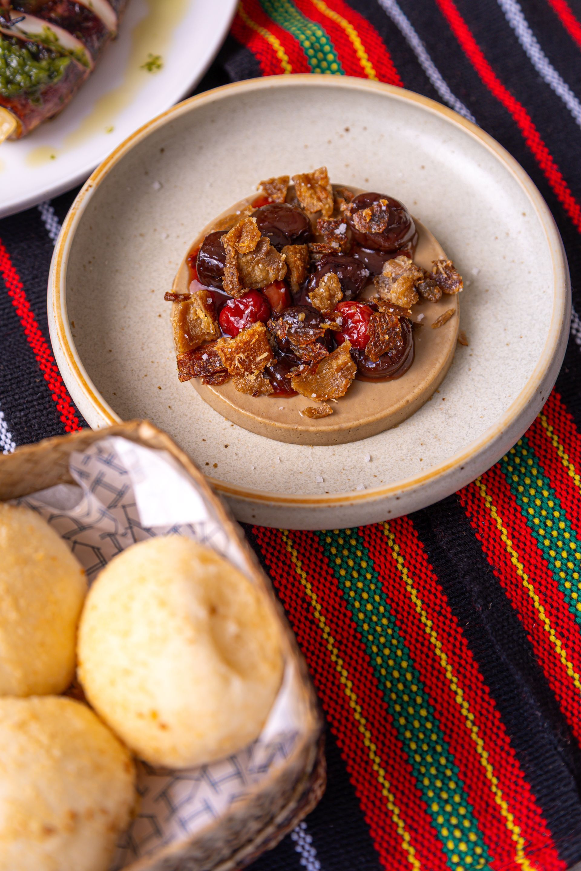 Small bowl of chunky chili or stew on a striped woven cloth, with bread rolls nearby