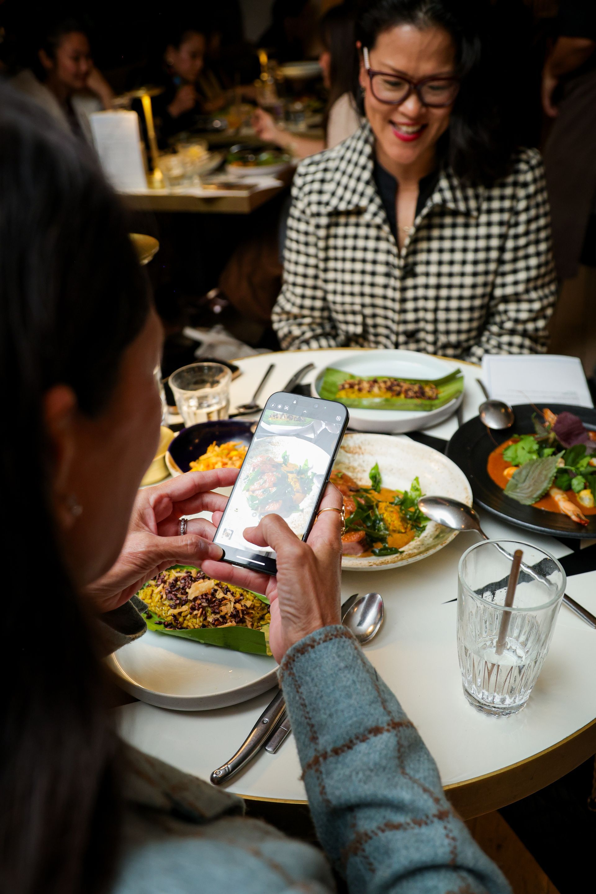 Friends sharing a meal at a restaurant, with one person taking a photo of the table spread
