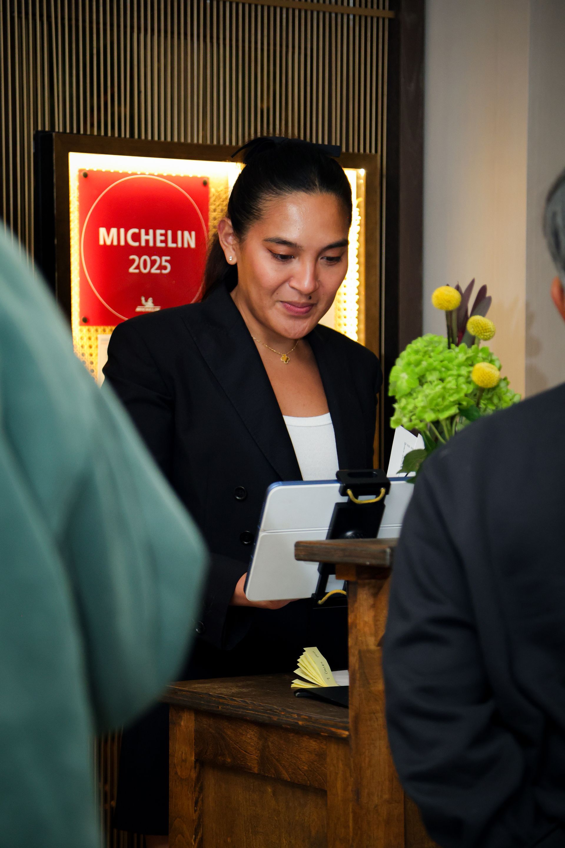 Receptionist at a hotel desk with a Michelin 2025 sign and flowers in the background