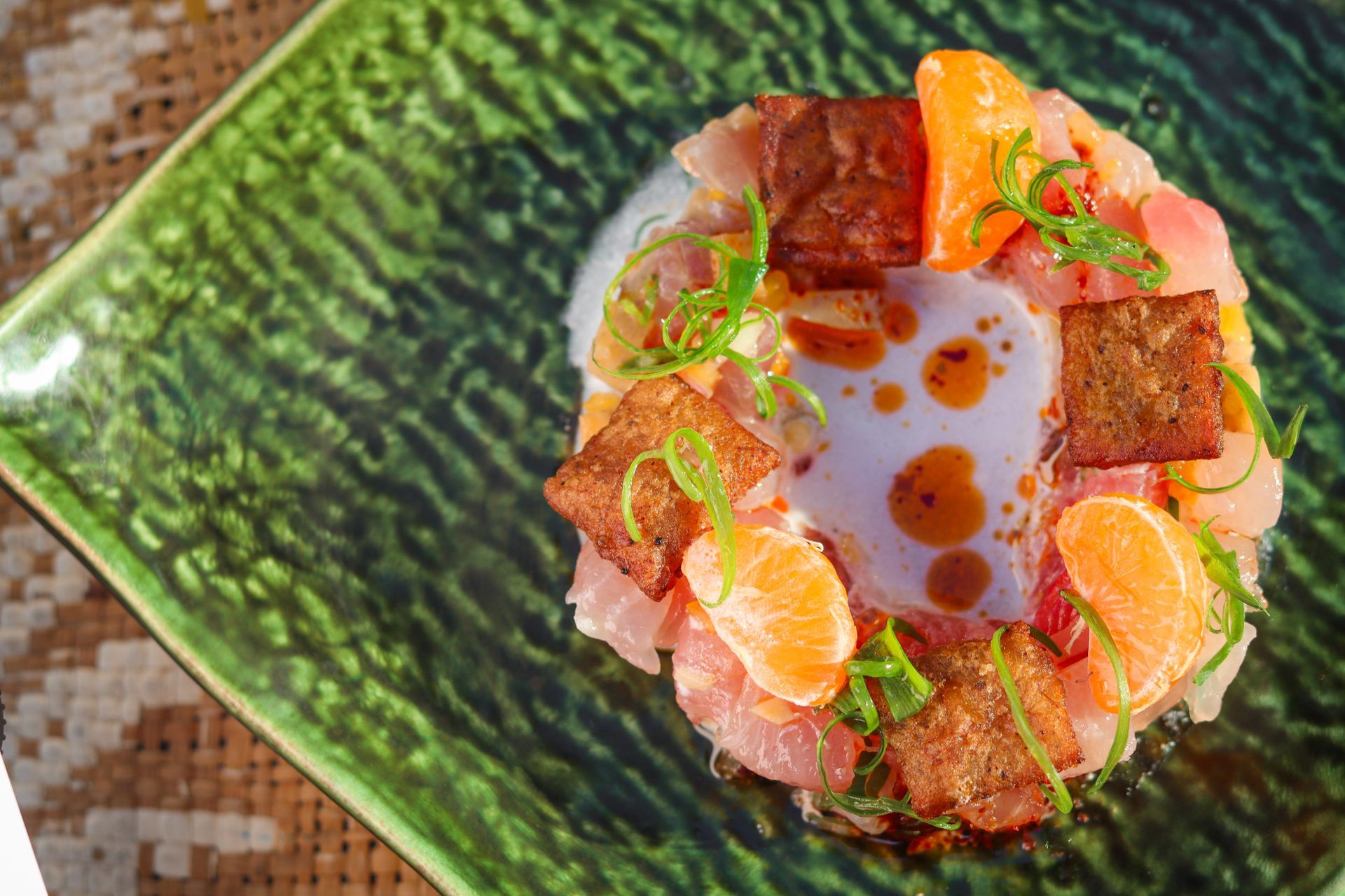 Overhead view of a plated dish with salmon, diced garnish, and sauce on a green textured plate
