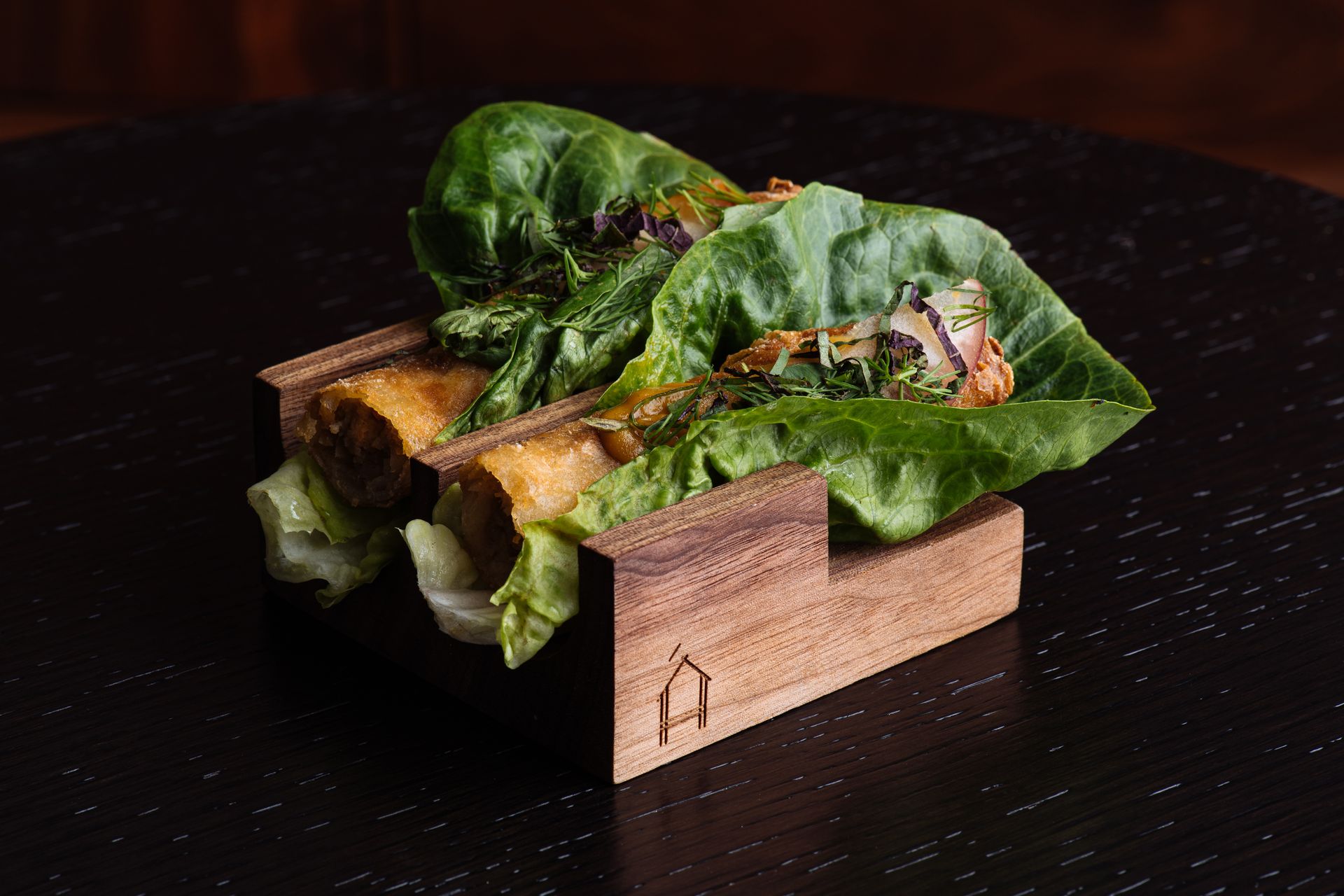 Leaves wrapped around grilled food in a small wooden tray on a dark surface