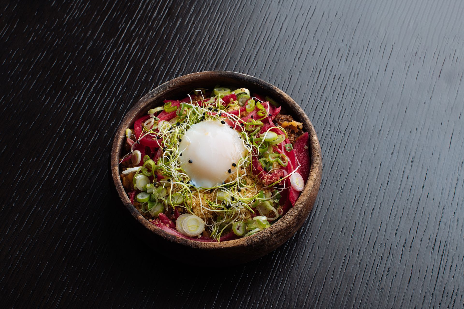 Bowl of colorful salad topped with a poached egg on a dark textured table