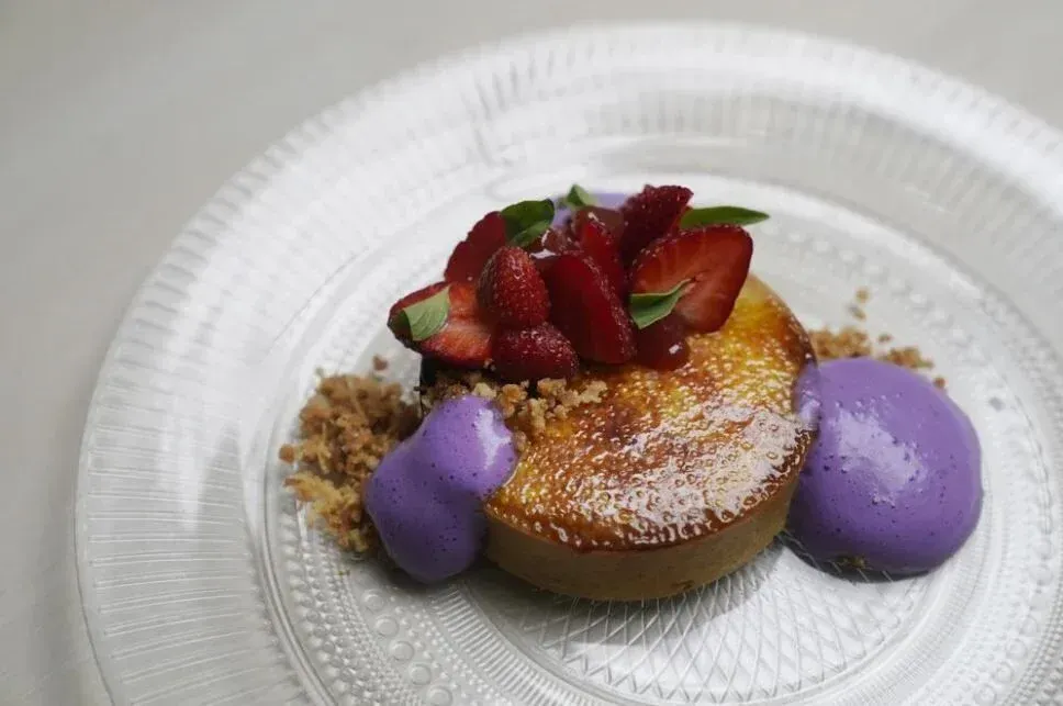 Dessert plate with a fruit tart, purple scoops, and strawberries on a white dish