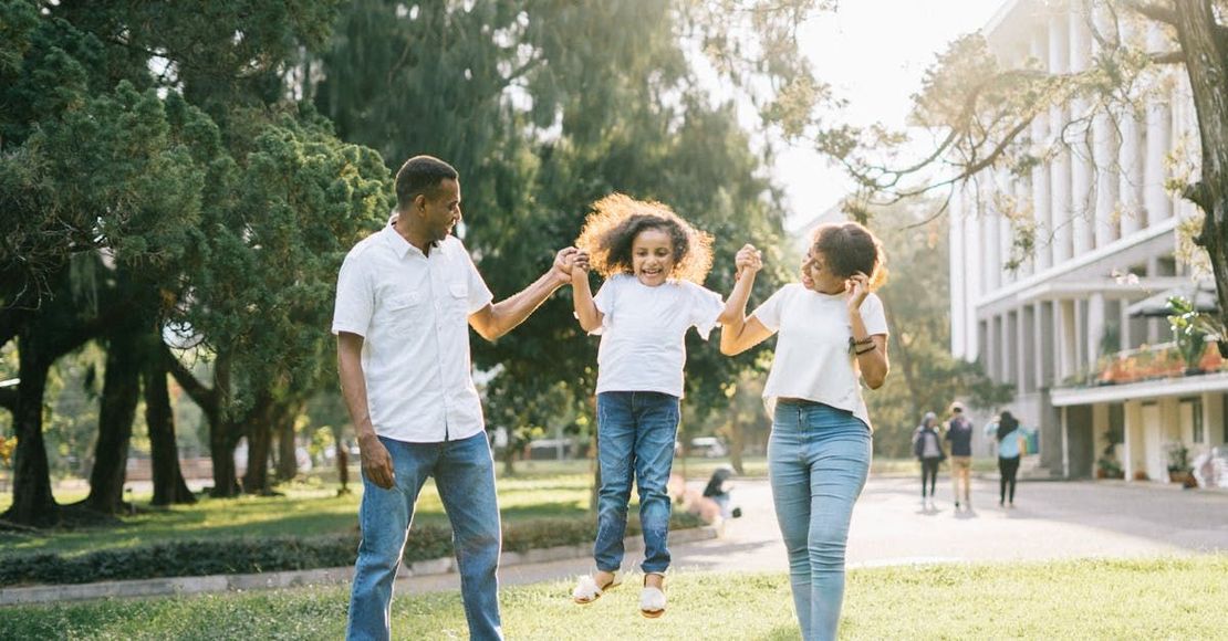 A family is holding hands and jumping in the air in a park.
