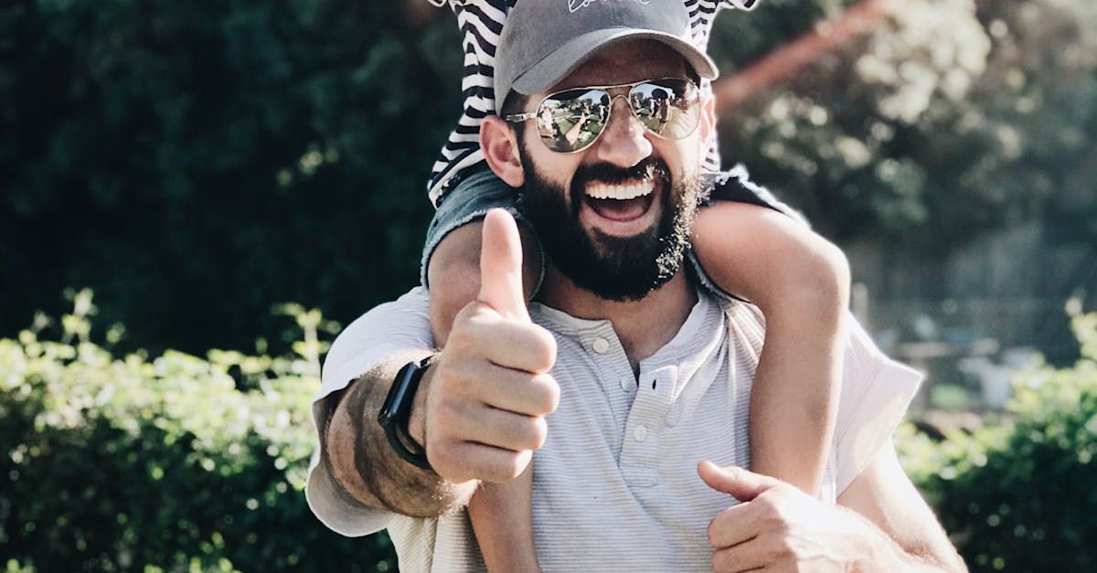 A man is carrying a little girl on his shoulders and giving a thumbs up.