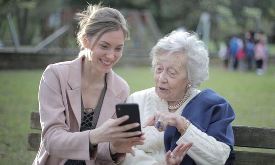 A young woman is teaching an older woman how to use a cell phone.