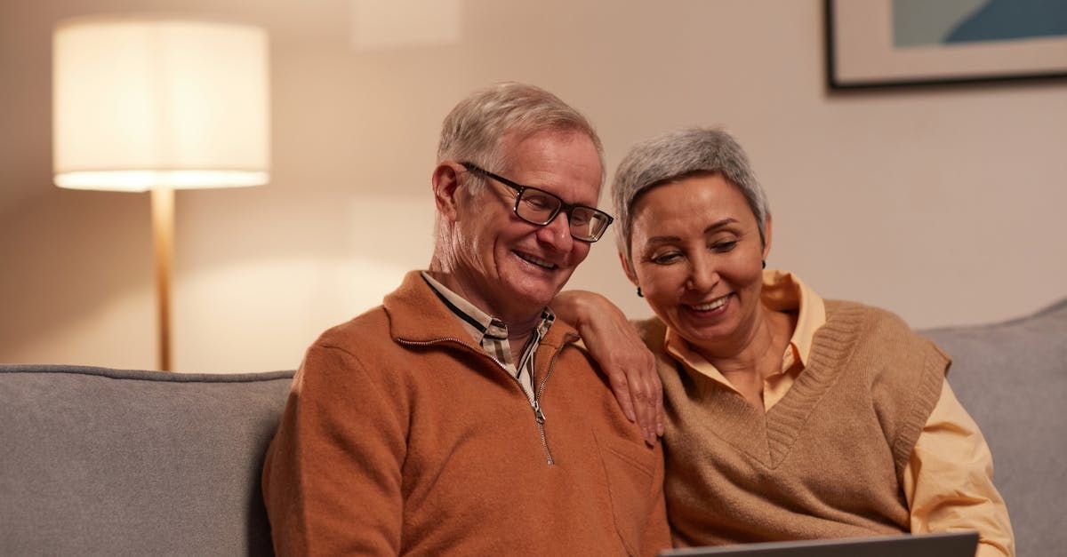 An elderly couple is sitting on a couch looking at a laptop.