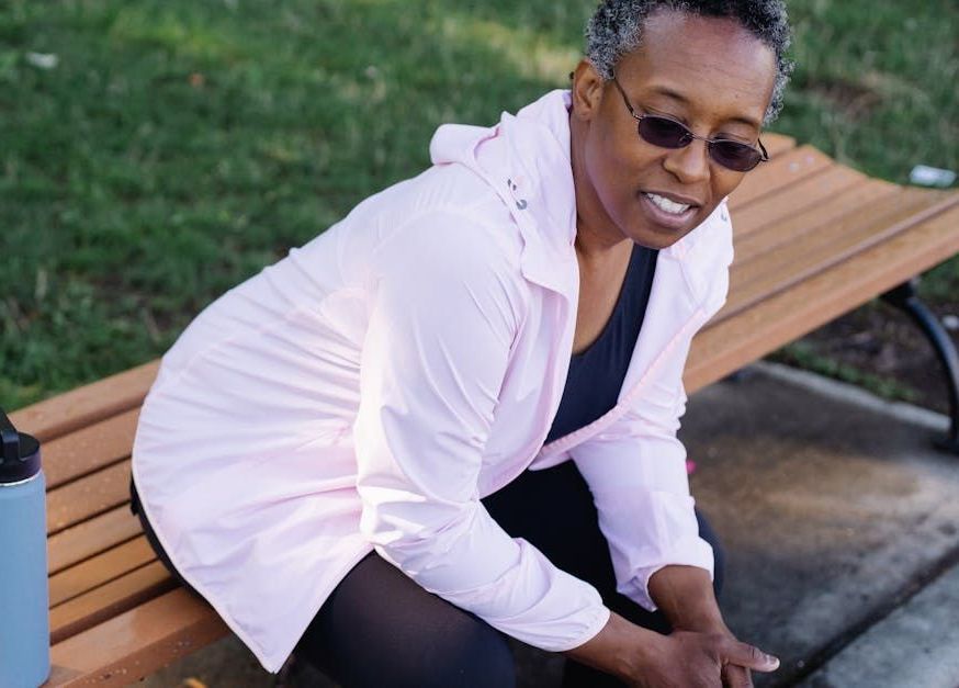 A woman is sitting on a park bench tying her shoes.