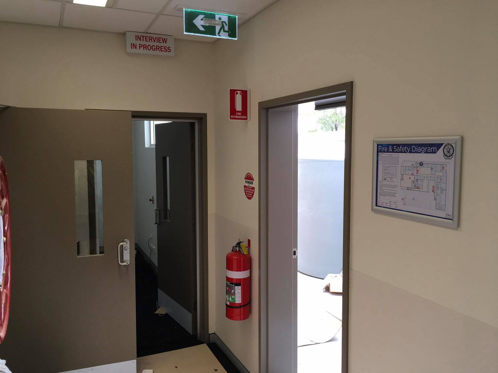 Hallway with open door, wall fire extinguisher, exit sign, and posted notices — Safe Industries Group in Woodrising, NSW