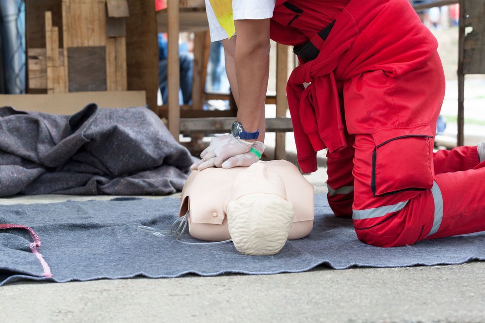 Rescue Worker Kneels Beside CPR Training Dummy on Mat During First Aid Practice — Safe Industries Group in Manning Valley, NSW