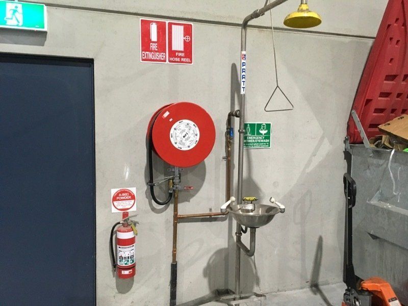 Red first aid kit mounted in a white hallway cabinet beneath an AED display — Safe Industries Group in Woodrising, NSW