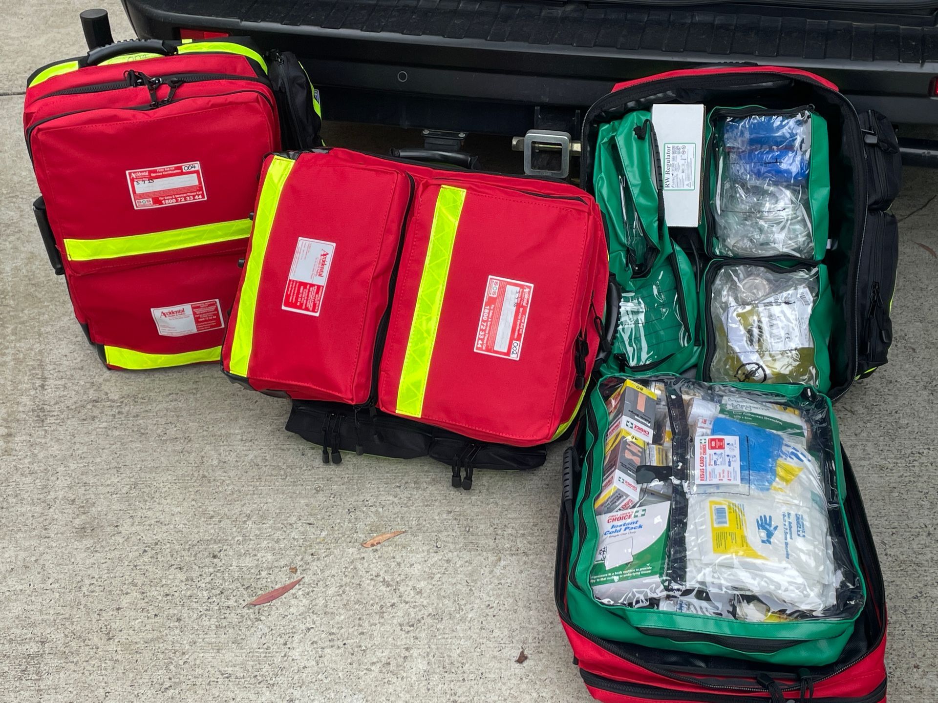 Open emergency supply bags with red and green medical kits on the ground near a vehicle — Safe Industries Group in Woodrising, NSW