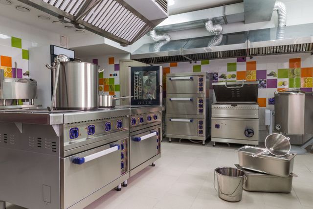 Commercial kitchen with stainless steel stoves, ovens, and pots under bright ventilation hoods