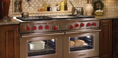 Stainless steel double oven with red knobs in a warm, wood-paneled kitchen