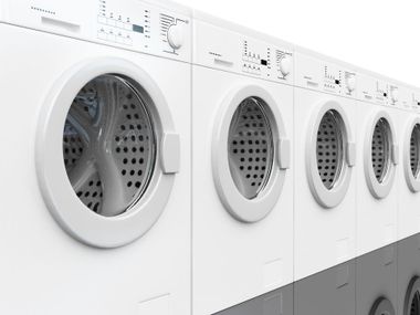 Row of white front-loading washing machines in a laundromat or laundry room