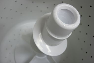 White plastic pipe fitting with threaded opening on a perforated metal surface