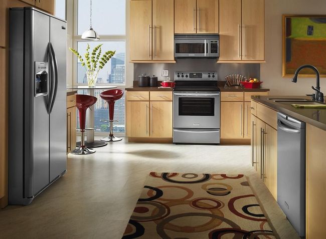 Modern kitchen with stainless steel appliances, wooden cabinets, and a small dining area by a window.