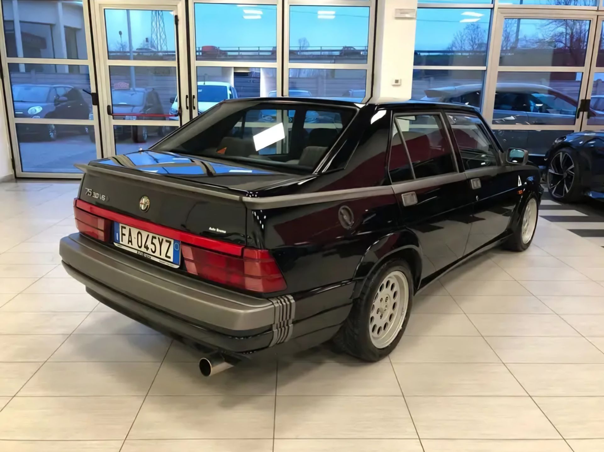 מכונית סדאן בצבע חום-אדום כהה של BMW באולם תצוגה, מבט מצד שמאל אחורי.