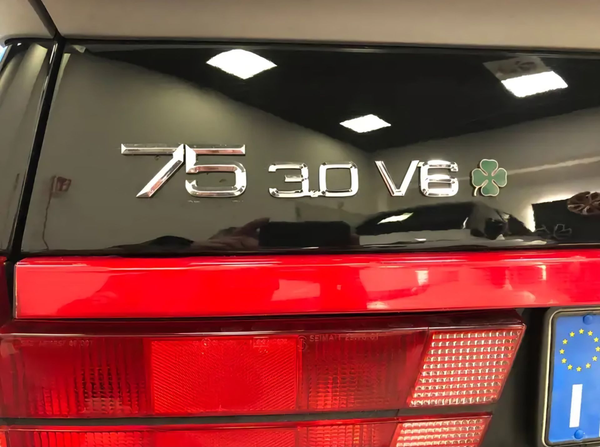 חלקו האחורי של אלפא רומיאו 75 3.0 V6 אדומה עם סמל כרום ופנס אחורי גלויים