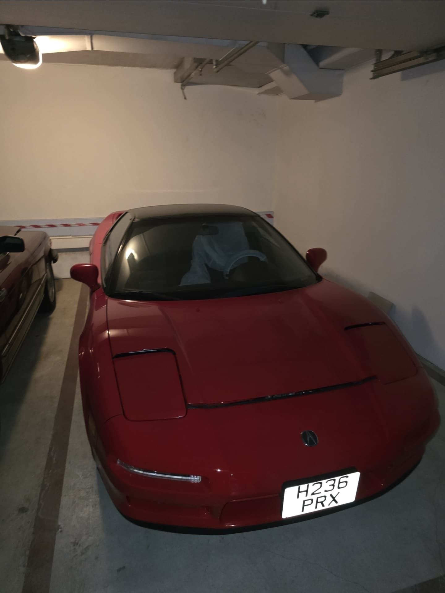 מכונית ספורט אדומה חונה במוסך, מבט מלפנים עם לוחית רישוי לבנה.