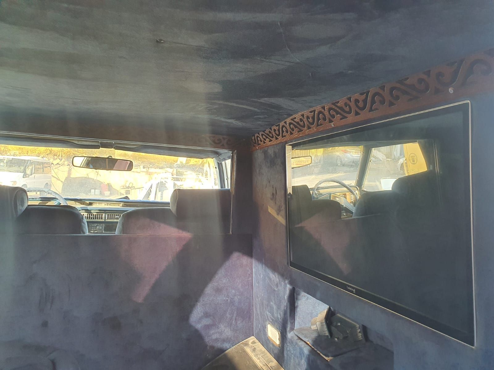 פנים הרכב עם טלוויזיה בעלת מסך שטוח גדול המותקנת על הקיר הימני ומבט דרך החלון האחורי.