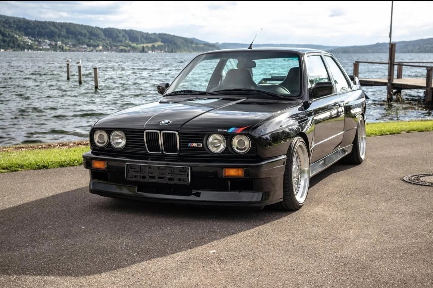 מכונית קופה שחורה של BMW חונה ליד כביש לצד אגם עם הרים ברקע
