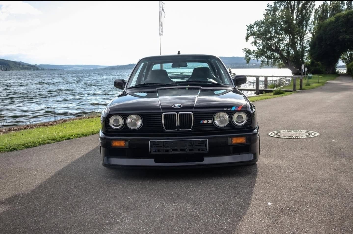 מכונית סדאן שחורה של BMW חונה על כביש לצד אגם כשברקע מים ועצים