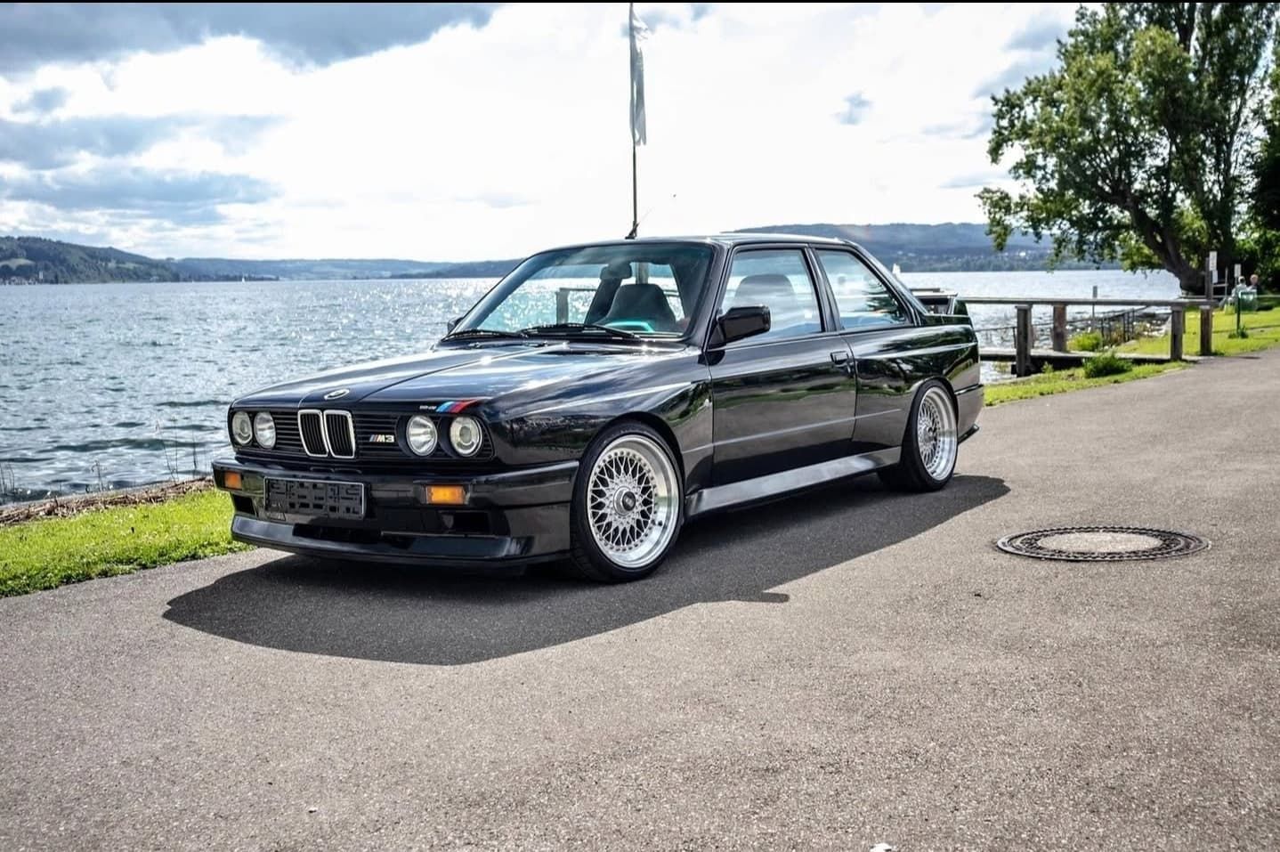 מכונית קופה קלאסית שחורה של BMW חונה ליד כביש על קו המים תחת שמיים בהירים
