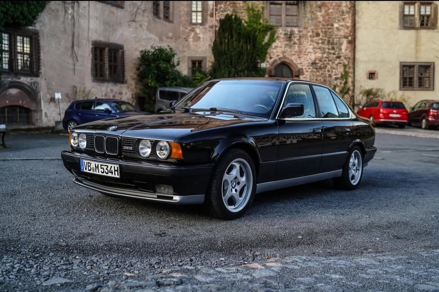מכונית סדאן שחורה של BMW חונה בחצר מרוצפת אבן ליד בנייני אבן