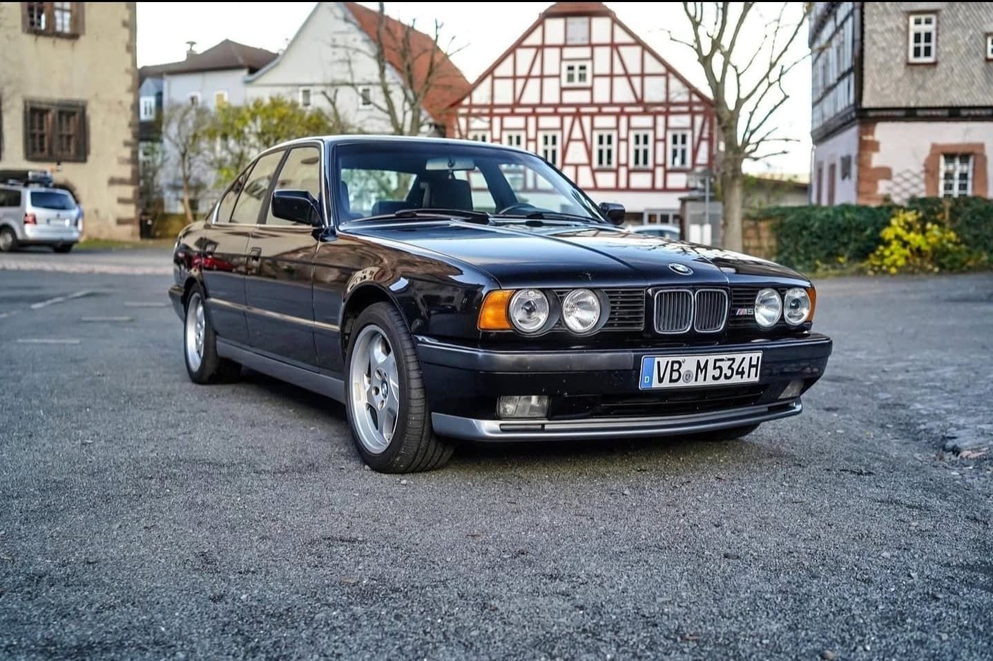 מכונית סדאן שחורה של BMW חונה ברחוב מרוצף באבנים מול מבנים היסטוריים