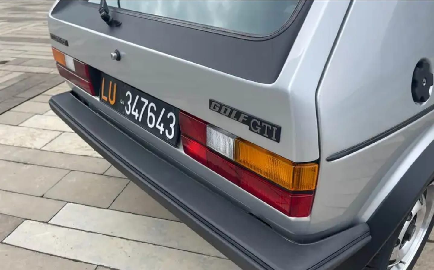 אחוריה של פיג'ו GTI האצ'בק כסופה עם לוחית רישוי שחורה, חונה על המדרכה.