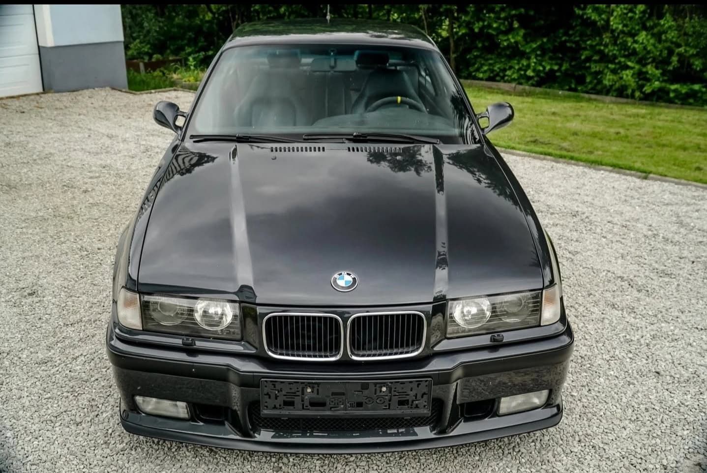 מבט קדמי של מכונית סדאן שחורה של BMW שחונה על שביל גישה חצץ.