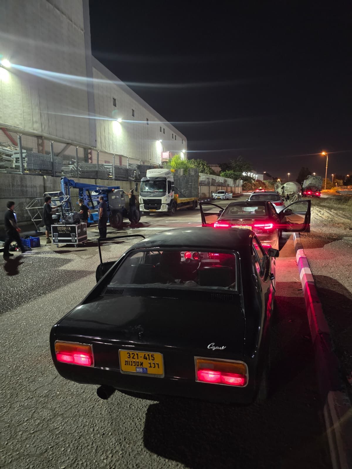 חניון לילי עם שורת מכוניות ליד כניסה מוארת למחסן