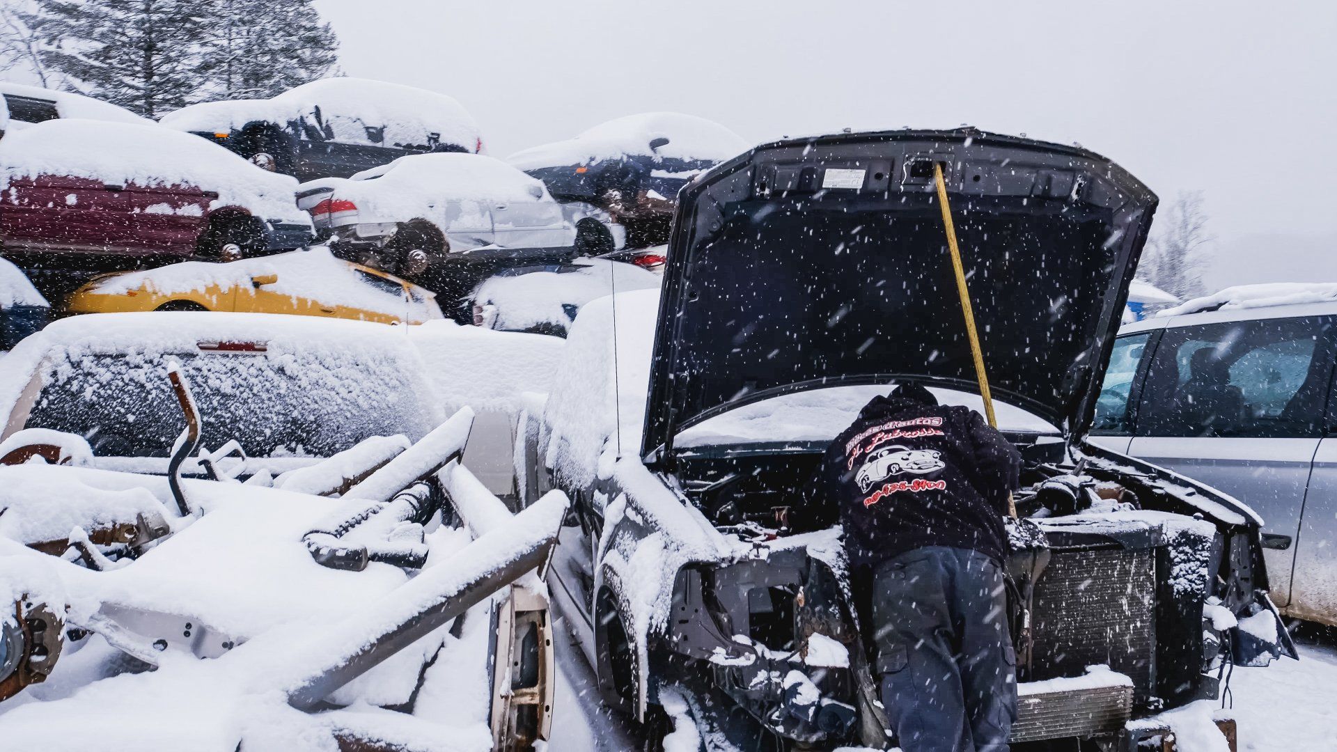 Une personne dans une casse, travaillant sur une voiture sous la neige.