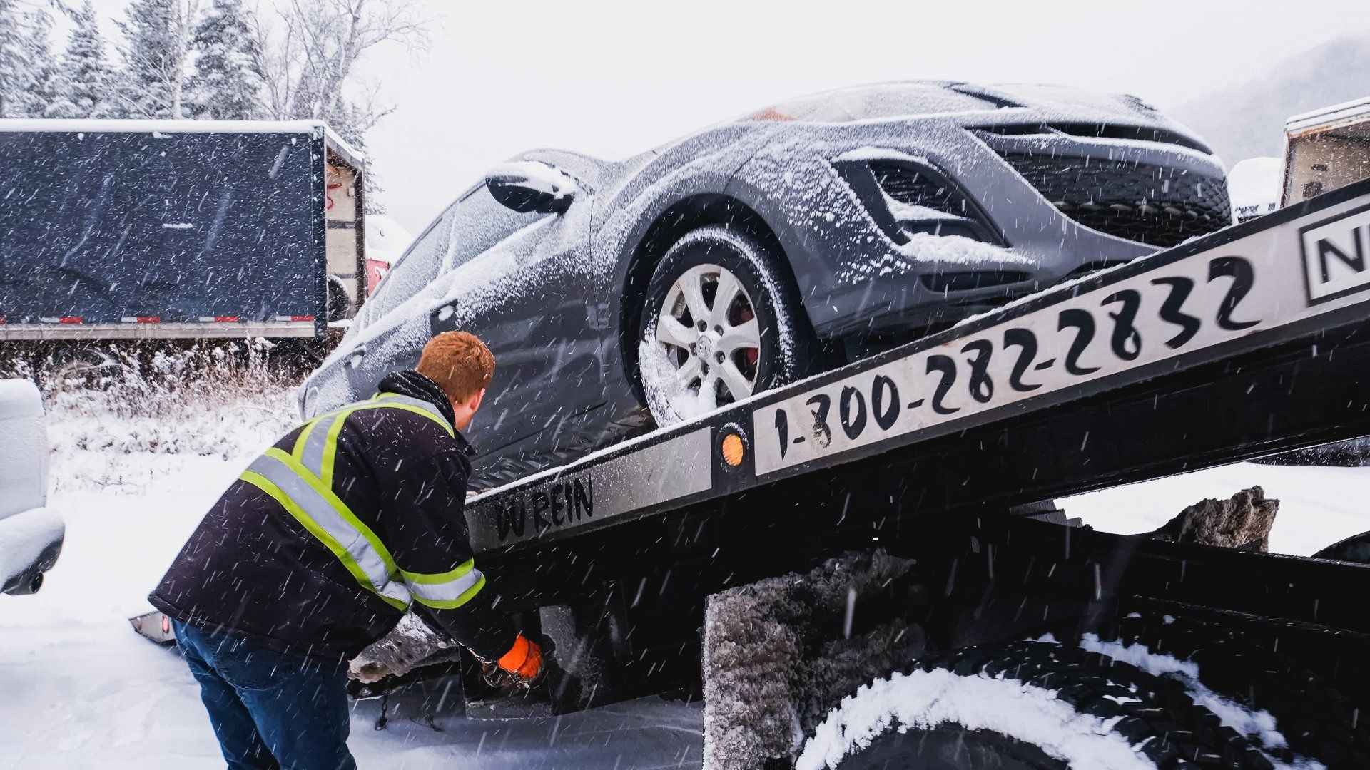 Un dépanneur sécurise une voiture grise sur un plateau dans un environnement enneigé.